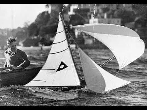 Historic photo of a Balmain Bug model yacht racing under sail beside its owner's rowing boat
